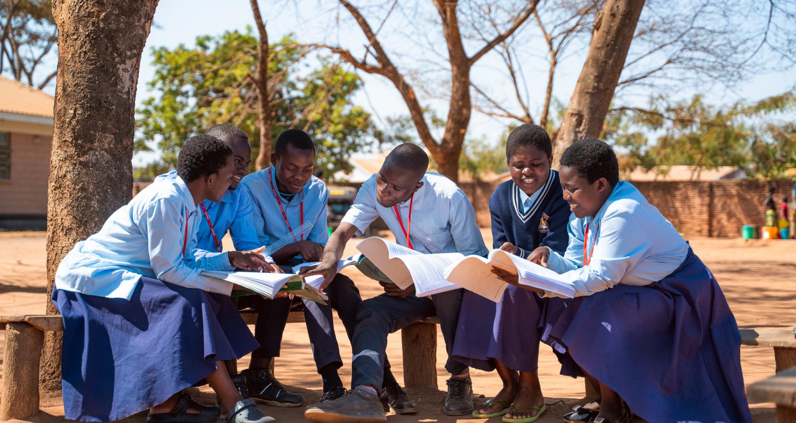 students at Sopa Community Day Secondary School in Mchinji District, Malawi, sit together on a bench reviewing their notes in preparation for their exams.