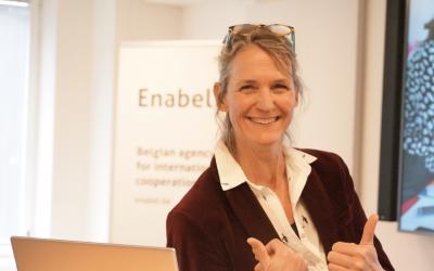 A woman in front of a laptop smiles and gives a thumbs up, signaling a positive response or success.