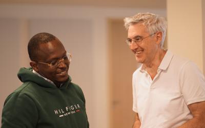 Two men wearing a white shirt and a green hoodie talking to each other in a casual setting.