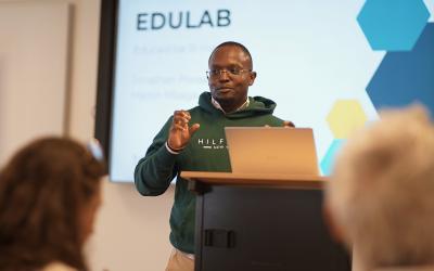 A man in a green hoodie stands at a podium, delivering a presentation to an audience.