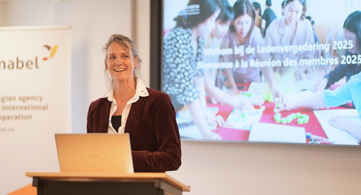 A woman stands at a podium, addressing an audience in front of a large presentation screen.