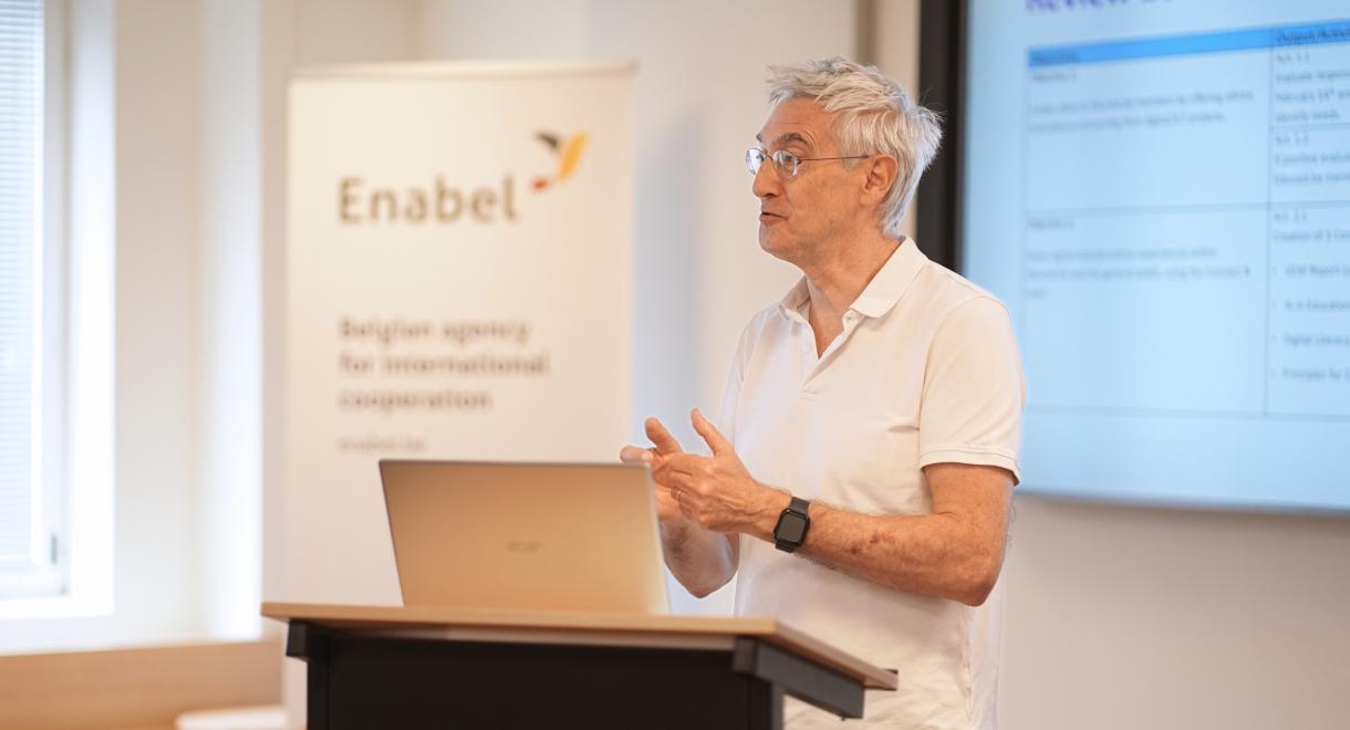 A man stands before a screen, delivering a presentation and engaging the audience with his gestures and expressions.