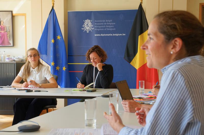 Drie vrouwen zitten in meeting rond een tafel. De meest rechtse vrouw spreekt.