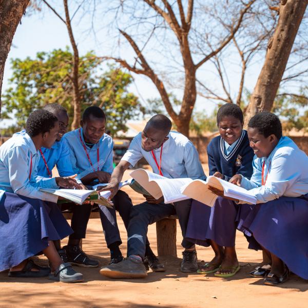 students at Sopa Community Day Secondary School in Mchinji District, Malawi, sit together on a bench reviewing their notes in preparation for their exams.