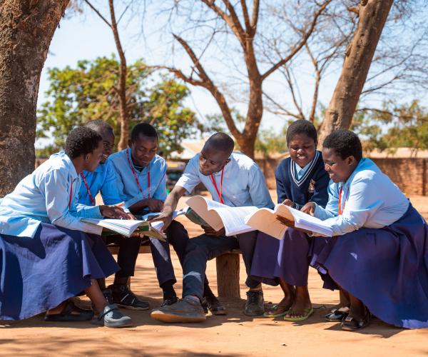 students at Sopa Community Day Secondary School in Mchinji District, Malawi, sit together on a bench reviewing their notes in preparation for their exams.